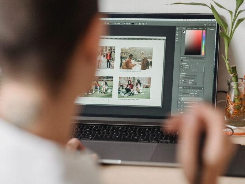 Back view of crop anonymous graphic designer with short hair in white shirt working on laptop using touchpad while retouching photos