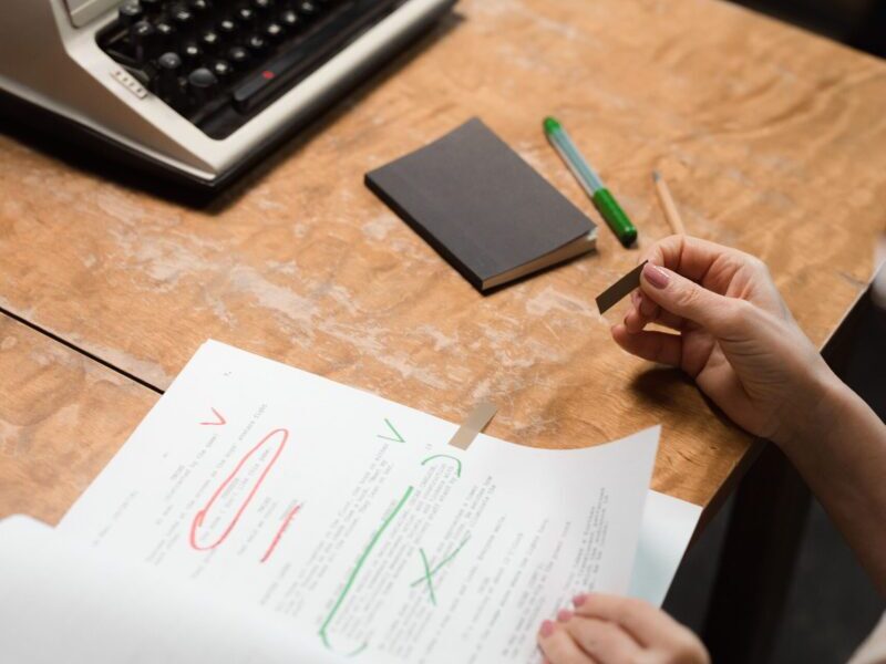 A person reviews a document at a desk with a retro typewriter, emphasizing office work in a vintage setting.